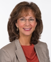 Professional woman with glasses smiling in a studio portrait.